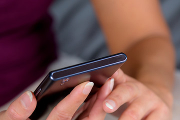 Woman sitting on bed and writing message on cellphone.