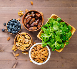Healthy vegan food - dry fruits, greens, nuts, berry. Superfoods on brown wooden background, top view.