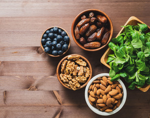 Healthy vegan food - dry fruits, greens, nuts, berry. Superfoods on brown wooden background, top view, copy space