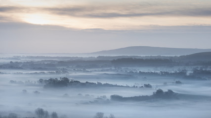 Obraz premium Stunning foggy English rural landscape at sunrise in Winter with layers rolling through the fields