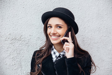 Smiling urban girl uses smart phone with smile on her face.Portrait of fashionable gir wearing a rock black style having fun outdoors