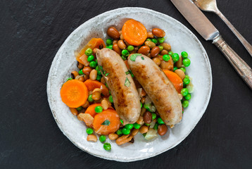 Sausage and bean casserole with carrots and green peas - top view