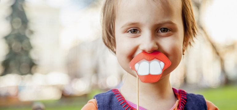 Humorous photo. Funny beautiful little child girl playing with fake lips and teeth.