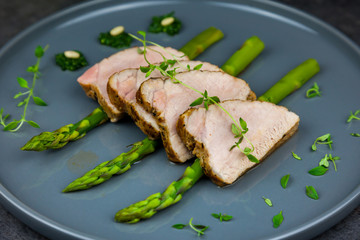 Slices of roasted pork tenderloin on asparagus with pesto from kale and thyme on the grey plate
