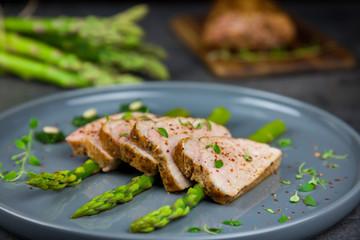 Slices of roasted pork tenderloin on asparagus with pesto from kale and thyme on the grey plate. Asparagus and all pork tenderloin on the background