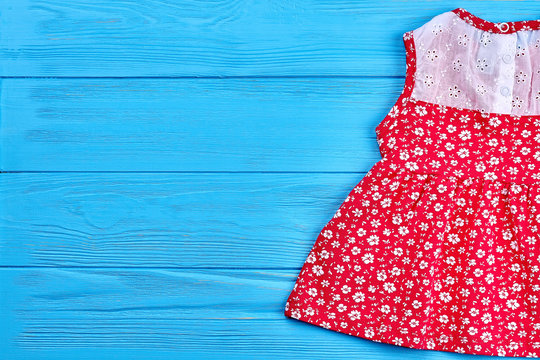 Cute Baby Dress And Copy Space. Short Red Summer Dress For Little Girls On Blue Wooden Background.