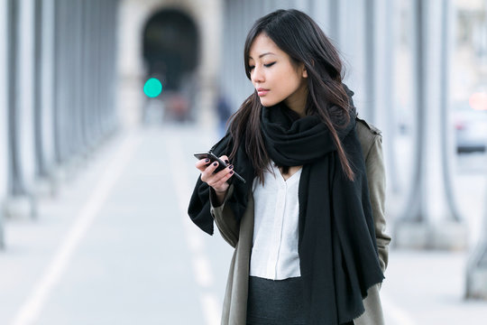 Concentrated Asian Young Woman Using Her Mobile Phone In The Street.