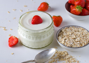White yogurt in glass bowl with spoon and starwberries on white background.