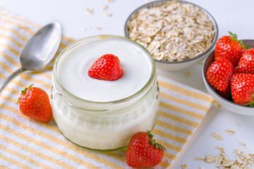 White yogurt in glass bowl with spoon and starwberries on white background.