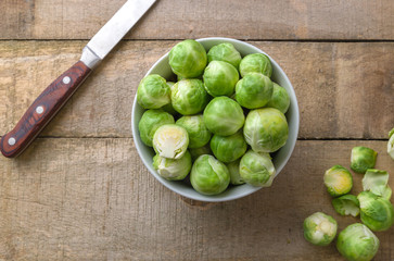Raw brussels sprouts in white bowl on wooden rustic desk.