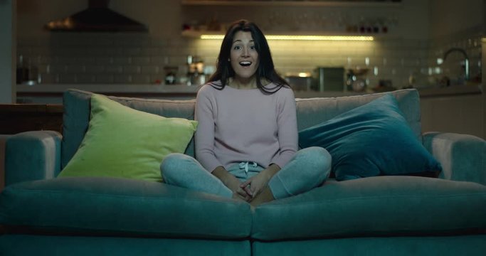 Woman sitting on a sofa is amazed and astonishment by what she is seeing tv