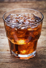 glass of cola with ice on wooden background