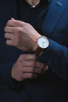 A dark portrait of a man dressed in an expensive suit, adjusting an elegant wrist watch