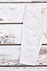 Kids white fashion trousers. Toddler boy white modern pants on wooden background, cropped image.