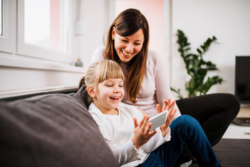 Playing games on smartphone. Little girl and her mother playing games on mobile phone at home.