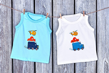 Infant boy t-shirts hanging on rope. Toddler boy clothes drying on clothesline on old wooden background.