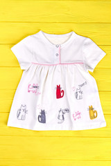 Babies white cat print dress. Infant girl short sleeve cotton dress on yellow wooden background. Kids brand outfit.