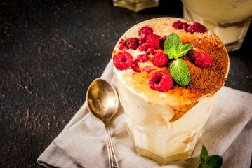 Three portioned glass with Italian dessert Tiramisu, with mint and raspberries, on dark rusty background.  Copy space