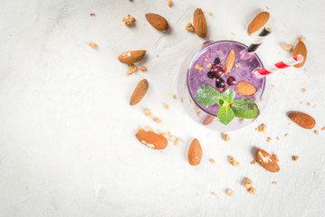 Healthy food. Dietary breakfast, snack. Berry smoothies with granola, black currant, blueberries and nuts almonds, decorated with mint. On a white concrete table with ingredients, copy space top view