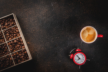 Concept of a cheerful, good start to the day, morning coffee. Dark rusty background with coffee beans, an alarm clock and a cup of coffee. Top view copy space