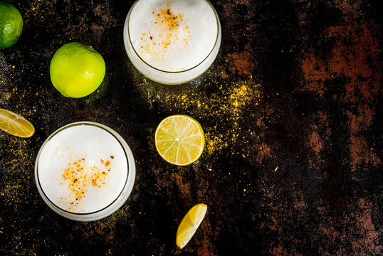 Peruvian, Mexican, Chilean traditional drink pisco sour liqueur, with fresh lime, on rusty black table, copy space top view
