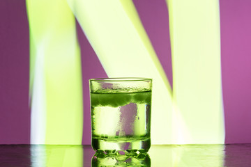Liquid with ice in a glass on a reflective surface on a reddish background