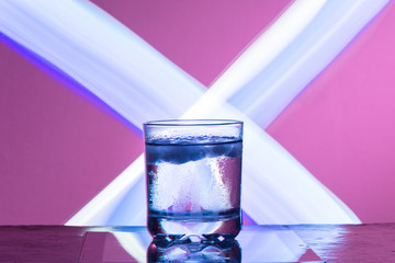 Liquid with ice in a glass on a reflective surface on a reddish background