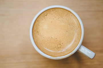Top view of white coffee cup filled with fresh hot espresso on wooden background