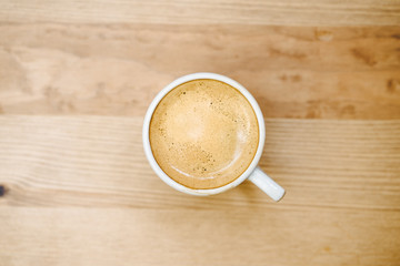 Top view of white coffee cup filled with fresh hot espresso on wooden background