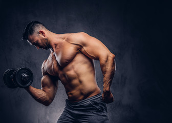 Fototapeta na wymiar Tall stylish shirtless bodybuilder dressed in sports shorts, doing exercise on a bicep with a barbell, standing in a studio.