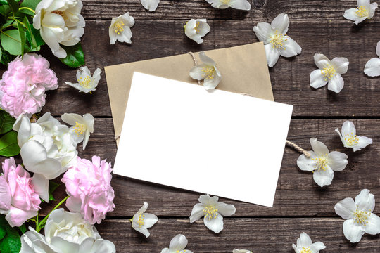 blank white greeting card in frame made of pink roses and white jasmine flowers and envelope on rustic wooden background