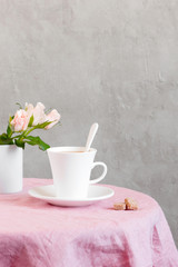 The white cup of tea or coffee with milk on the table coated with pink tablecloth