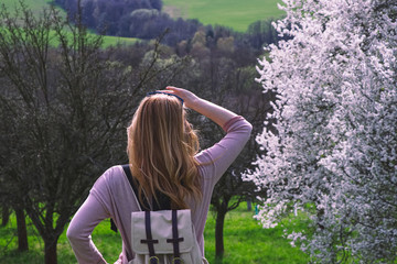 Woman traveler standing in blossoming orchard at springtime 