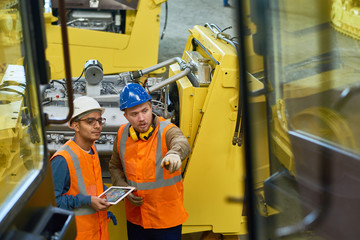 Bearded industrial engineers wearing protective helmets and reflective vests using digital tablet...