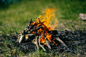 Burning firewood in outdoor summer camp on green abstract background. Travel and tourism. Nature leisure rest. Wood in flame. Lifestyle cozy place for dinner preparation. Smoldering coals and ash.