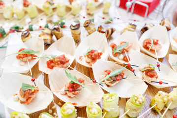 Delicious shrimp and sliced tomatoes on a wooden boat. Zucchini rolls with pine nuts. Tasty buffet table. Summer party outdoor. Catering concept