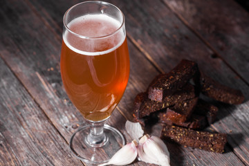 A glass of light beer and fried hot aromatic garlic toasts of black bread on a table made of textured old wooden boards