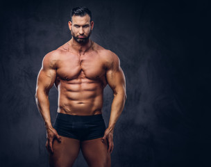 Obraz na płótnie Canvas Portrait of a shirtless tall huge male with a muscular body with a stylish haircut and beard, in a underwear, posing in a studio.