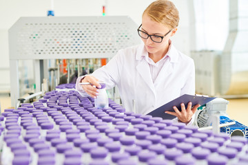 Highly professional technologist wearing eyeglasses and white coat checking quality of soy milk while standing at conveyor belt of dairy factory