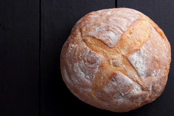 Round bread on a black background, bread from a stove on dark boards, a dough for a designer, copy space, rustic style, minimalism, top view, bakery