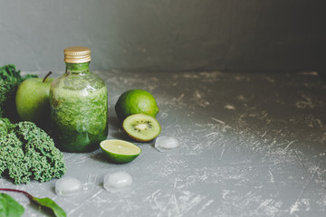Healthy green smoothie with ingredients and ice cubes on gray background