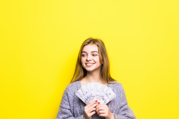 Joyful teenage girl with dollars in her hands isolated on yellow background