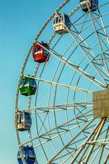 Ferris wheel with multicolored cabins, sunny day, blue sky
