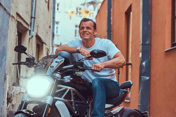 Fototapeta na wymiar A handsome brutal biker, ride on a motorcycle, in a narrow old Europe street.