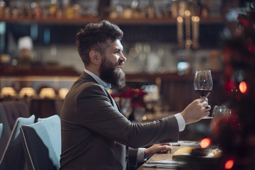 Portrait of handsome young man smiling and holding glass of red wine over blurry background
