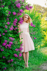 Naklejka premium slender beautiful girl in beige dress, in a blossoming garden in spring, elegant blonde girl in a dress outdoors with lilac flowers