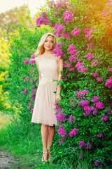 slender beautiful girl in beige dress, in a blossoming garden in spring, elegant blonde girl in a dress outdoors with lilac flowers