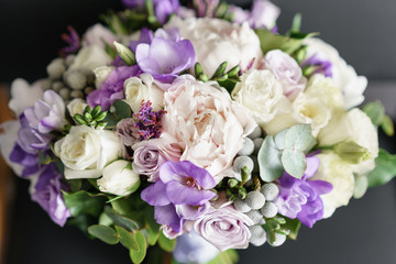 Brides wedding bouquet with peonies, freesia and other flowers on black arm chair. Light and lilac spring color. Morning in room