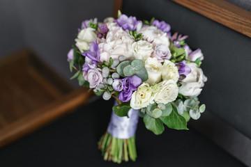 Brides wedding bouquet with peonies, freesia and other flowers on black arm chair. Light and lilac spring color. Morning in room