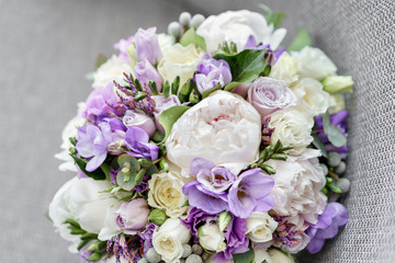 Brides wedding bouquet with peonies, freesia and other flowers on black arm chair. Light and lilac spring color. Morning in room